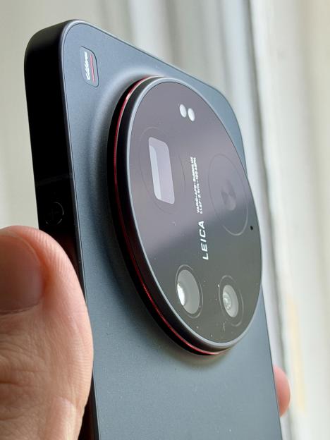 A hand holding a Xiaomi phone, showing its back with a prominent circular camera module containing multiple lenses and a red ring accent.