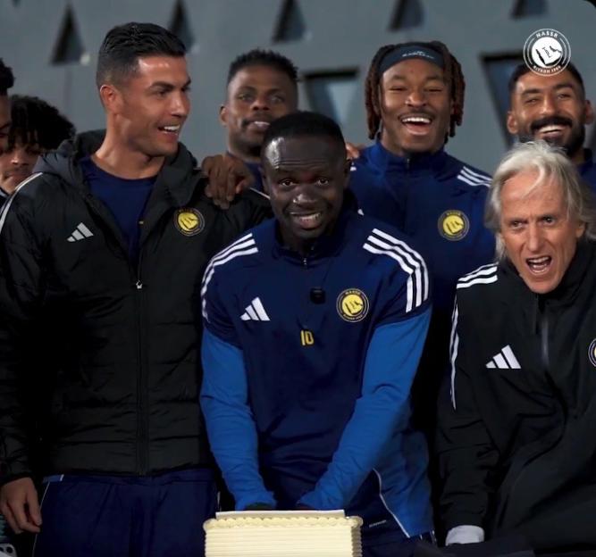 Footballers and coaches celebrating a birthday with a cake.