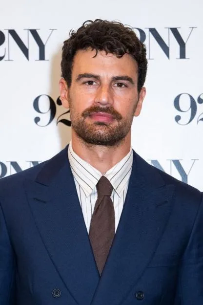 Theo James wearing a blue suit, striped shirt, and brown tie for Netflix's "The Gentlemen."