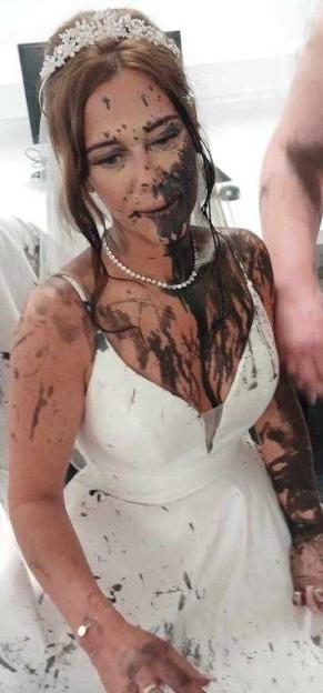 A bride splattered with black paint on her wedding dress and face.