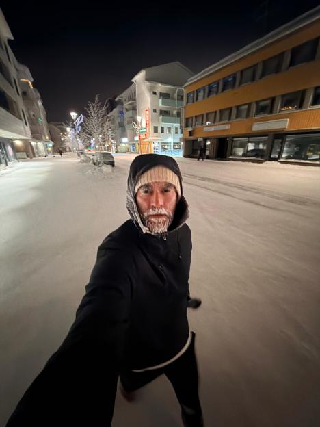 A man's frozen bearded face appears in a selfie on a snow-covered street in Lapland.