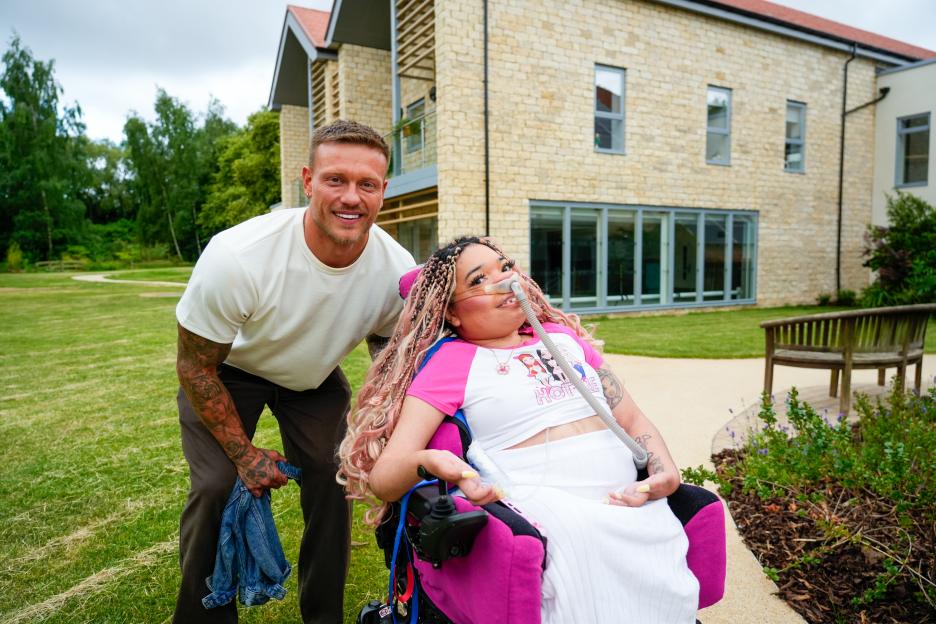 Alex Bowen posing next to a young woman in a wheelchair outside a children's hospice.