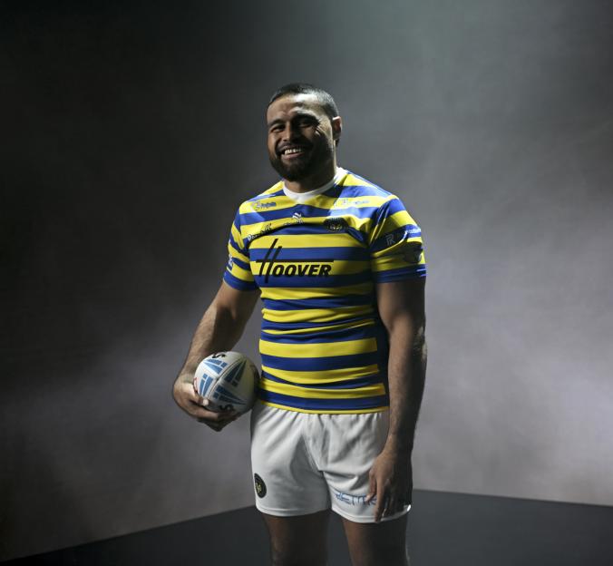 Toafofoa Sipley in a yellow and blue striped Warrington Wolves rugby jersey, holding a rugby ball.