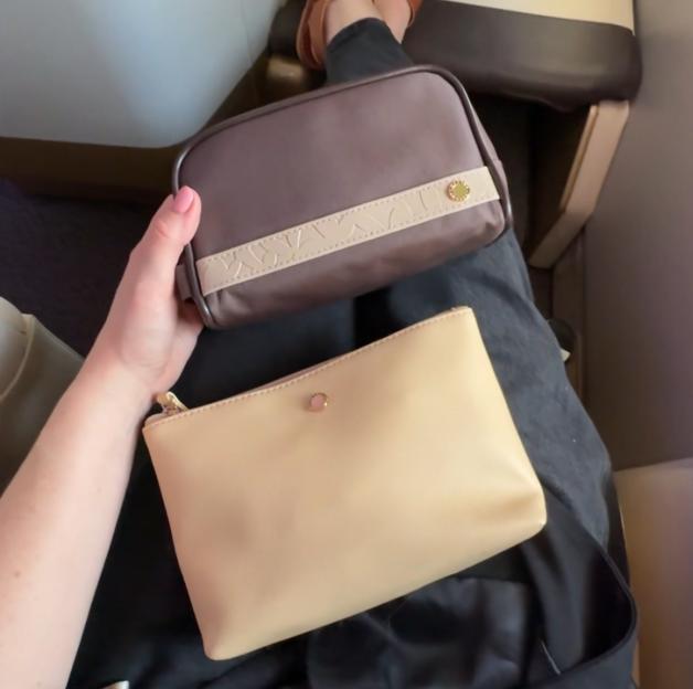 A person's legs and hands with two small bags in an airplane seat.
