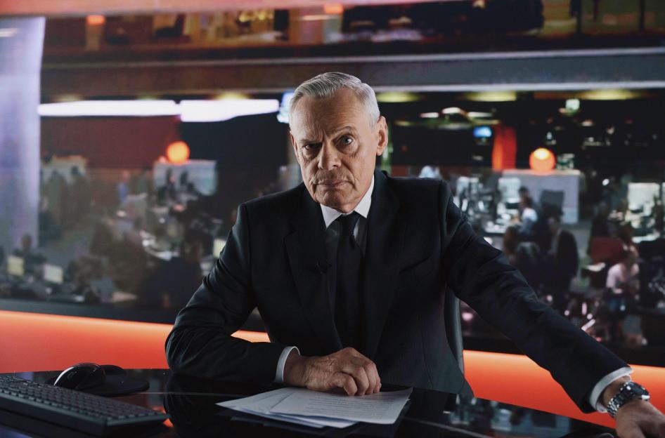Martin Clunes as Huw Edwards on a television set.