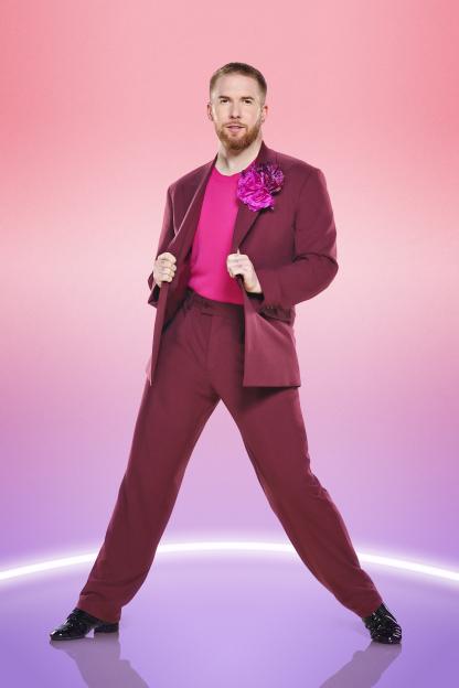 Neil Jones in a maroon suit and pink shirt, striking a dance pose.