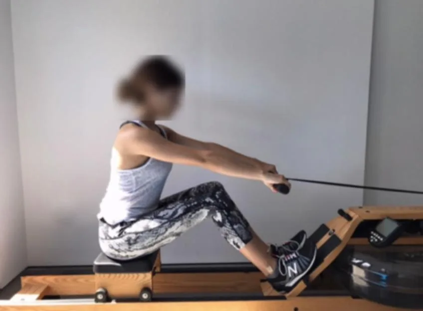 A woman with a blurred face uses a rowing machine.