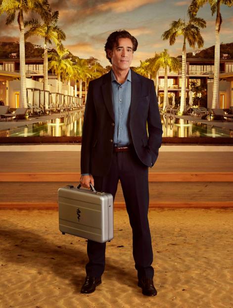 Man in a suit holding a briefcase with a Caduceus symbol, standing on sand in front of a resort with palm trees.