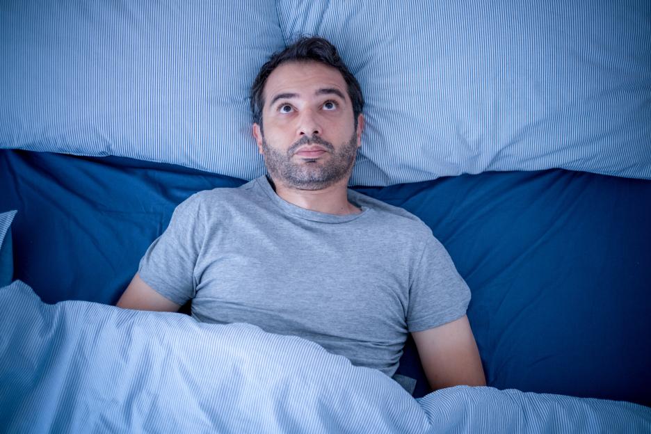 Anxious man lying awake in bed, unable to sleep.
