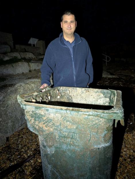 Ryan Stalker stands beside a plastic wheelie bin with "Baldwin County, Alabama" written on it and goose barnacles attached, which washed ashore in England after traveling from the USA.