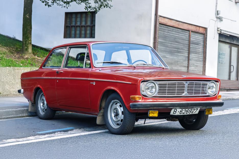 A red 1970 Volvo 142 sedan parked on a city street.
