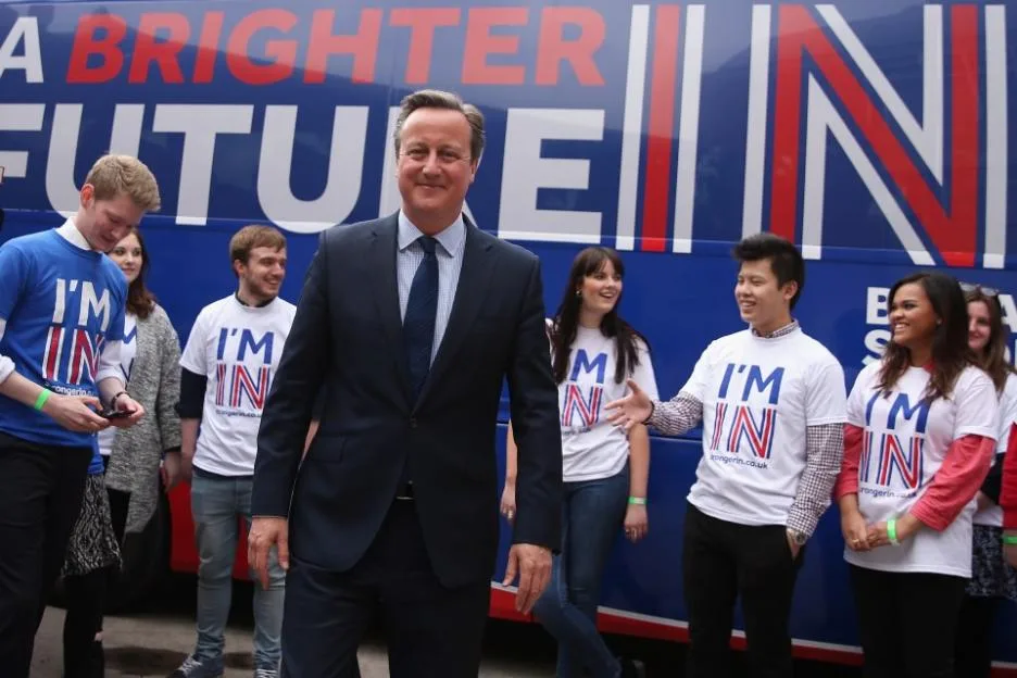 Prime Minister David Cameron stands in front of a "Brighter Future In" campaign bus surrounded by students.