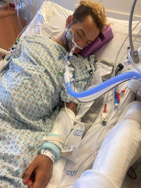 Gene Long, recovering in a hospital bed with medical tubes and wires attached, after waking from a two-month coma.