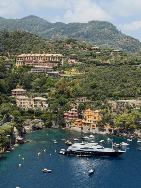 Coastal town of Portofino, Italy, with large yachts and small boats in the bay below terraced hillsides with buildings and lush greenery.