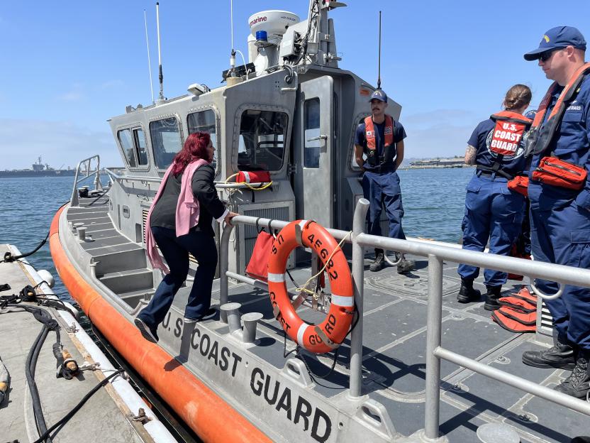 A woman stepping onto a U.S. Coast Guard boat, with three Coast Guard personnel on board, in San Diego Bay.