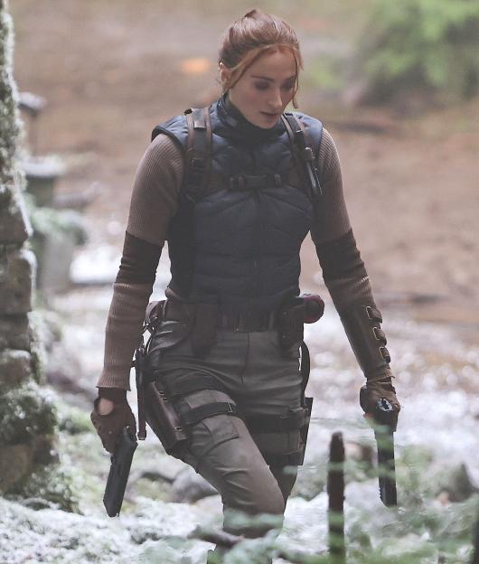 Sophie Turner as Lara Croft holding two pistols while filming Tomb Raider.