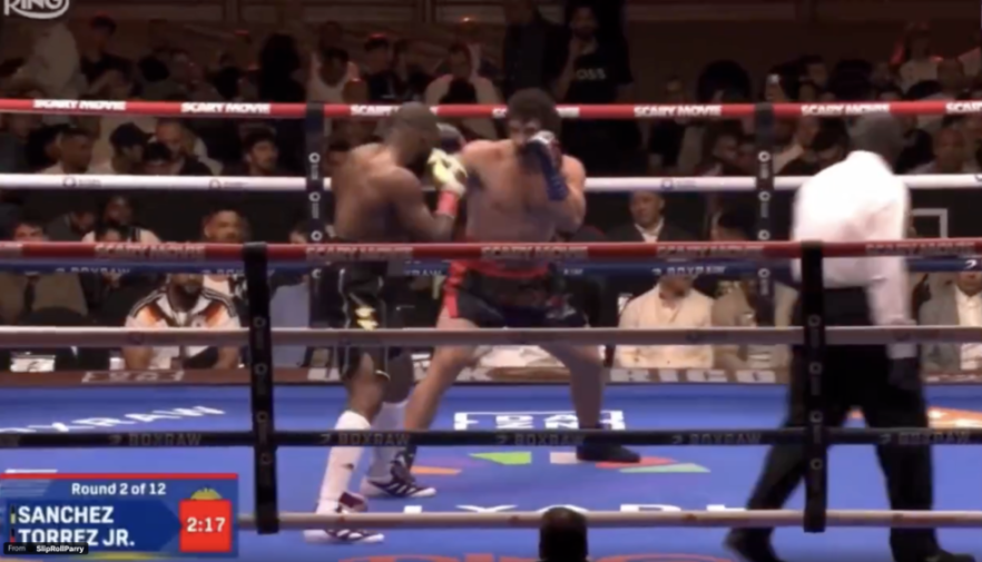 Two boxers, one in black shorts and the other in red, are in the ring during Round 2 of 12.