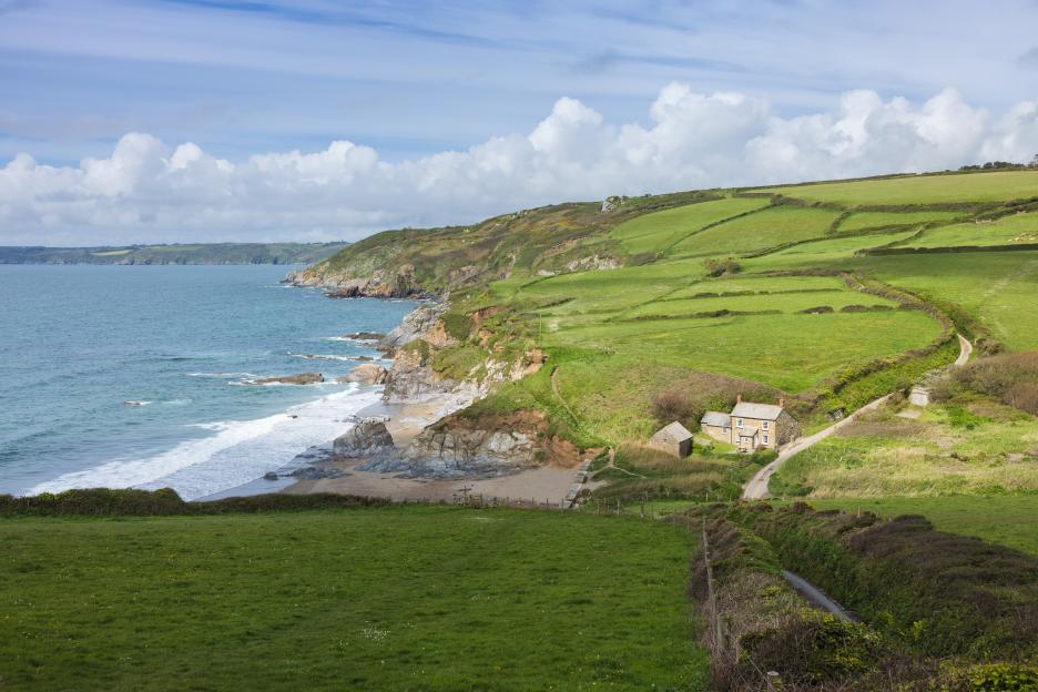 View of the coast in Dorset, England, with green fields, a stone house, and a road winding down to a small beach.