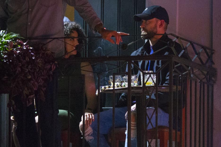 Justin Timberlake and Alisha Wainwright sitting at a table with drinks on a balcony.