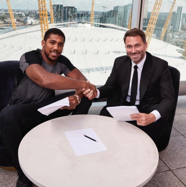 Anthony Joshua and Eddie Hearn shaking hands after signing a contract.