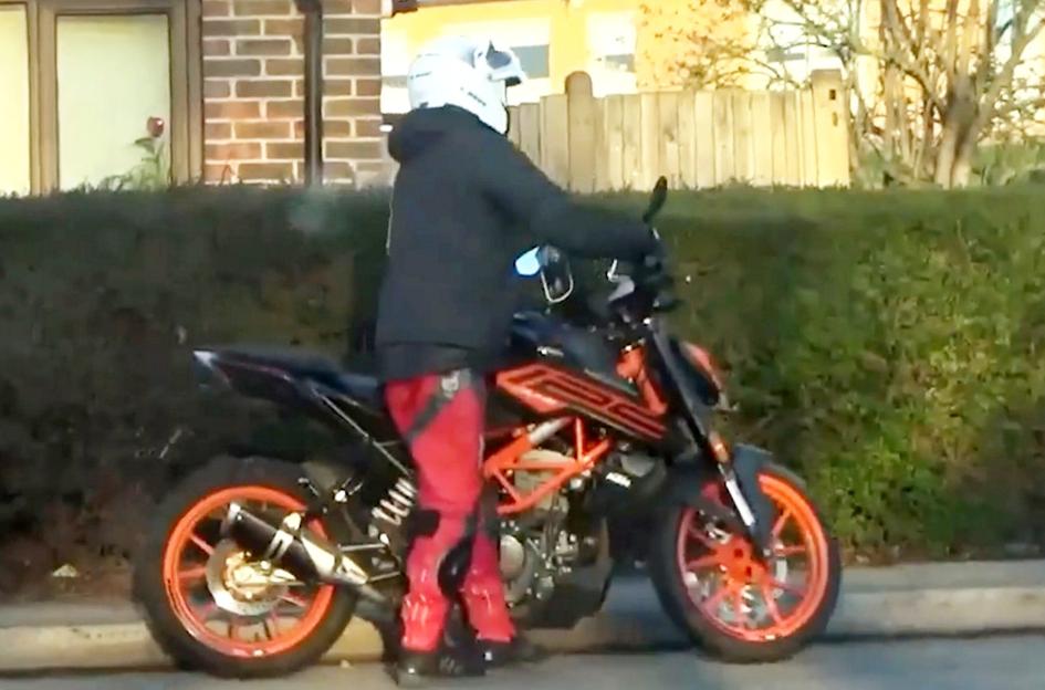 Man in a helmet and red pants riding a black motorbike with orange wheels.