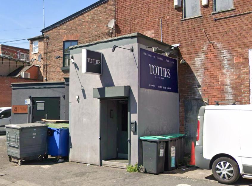 Tottie's bar, Altrincham, with signs for "Totties Late Bar" and two glass recycling bins next to the entrance.