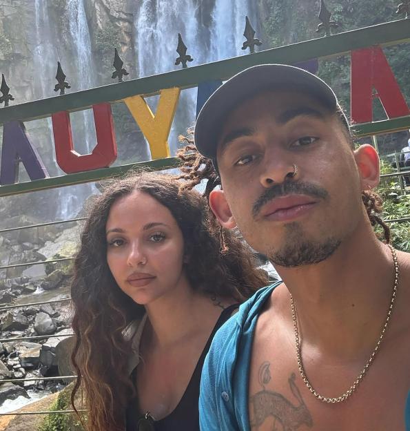 Jade Thirlwall and Jordan Stephens take a selfie in front of a waterfall, with a colorful "NAUYACA" sign in the foreground.