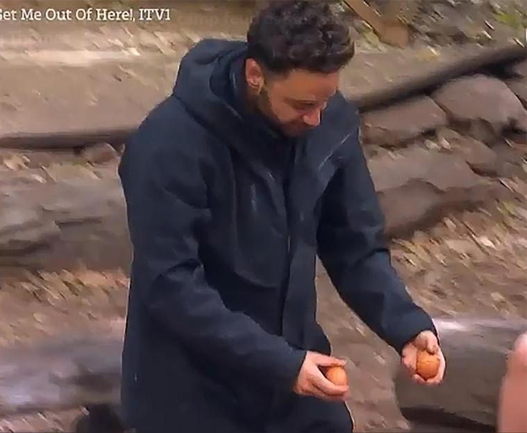 A man wearing a black coat holds two oranges in his hands.