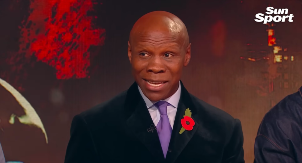 Chris Eubank wearing a black coat, a purple tie, and a red poppy pin.