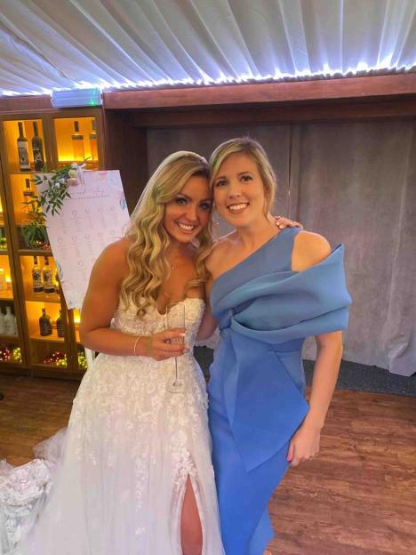 Amy Dowden in a white wedding gown, holding a champagne glass, with a friend in a blue dress.