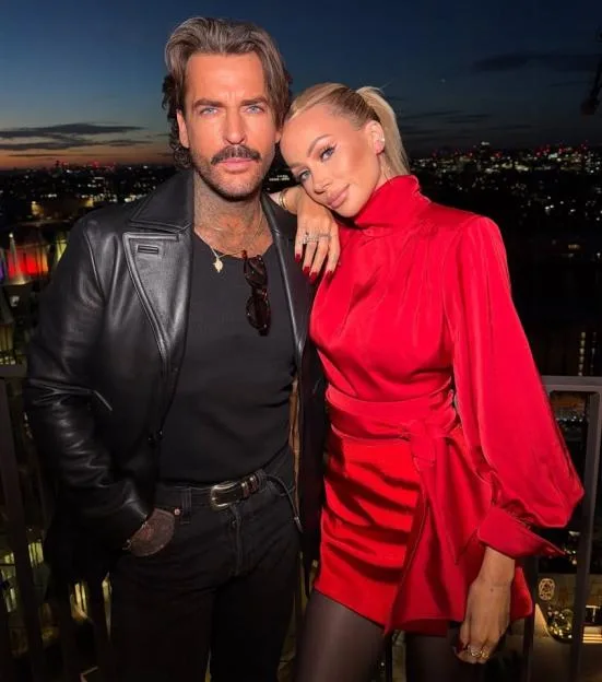 Olivia Attwood and Pete Wicks posing together at dusk with a city skyline in the background.
