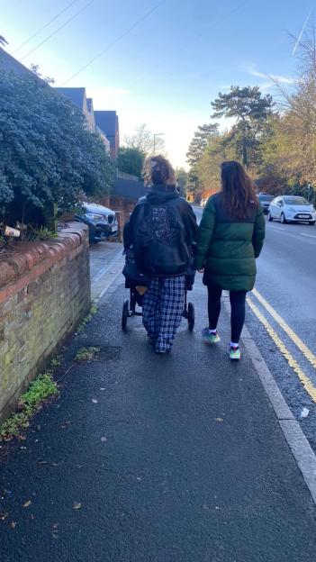 Two people walk down a sidewalk, one pushing a stroller.