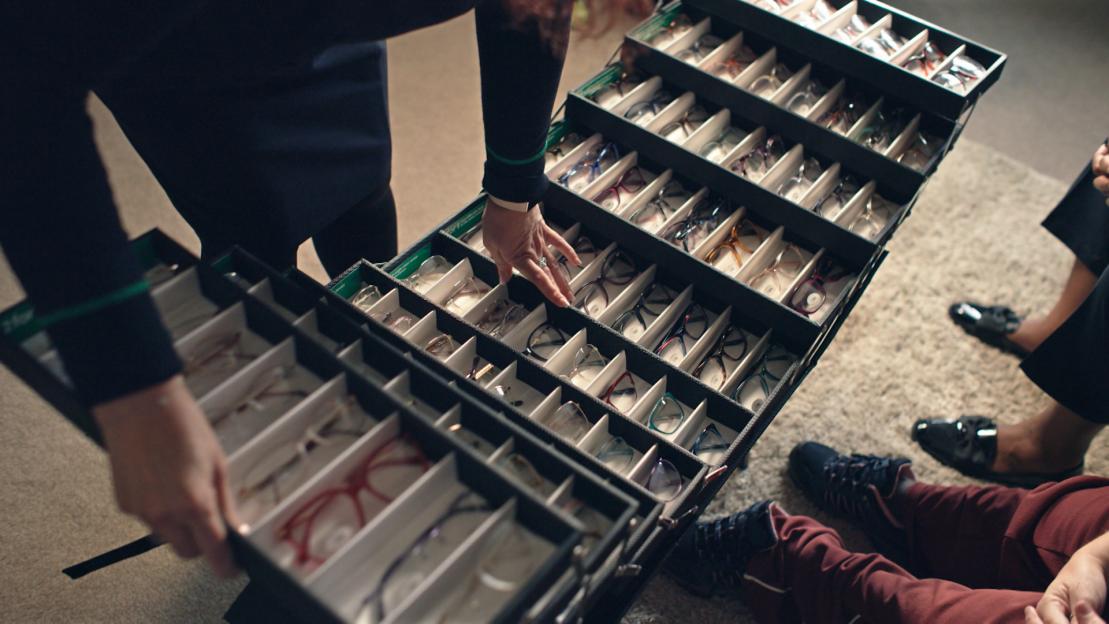 A person reaching into an open case filled with many pairs of eyeglasses.