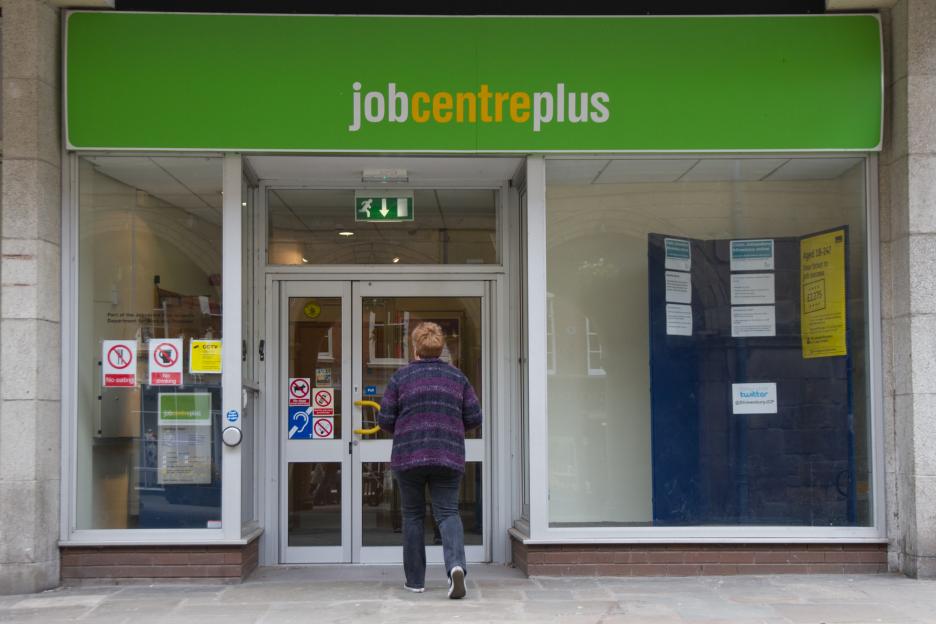 A woman in a striped sweater walks towards the entrance of a Jobcentre Plus building.