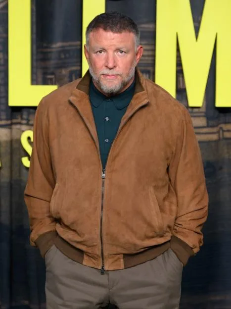Guy Ritchie wearing a brown suede jacket and dark green shirt.