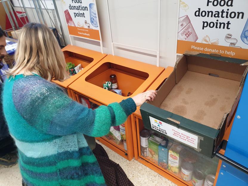 A person in a blue and green striped sweater depositing items into a food donation box.