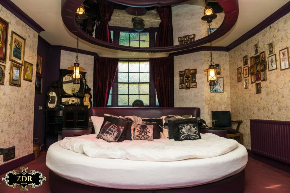 A bedroom in Naughty Narnia with a round bed, map-patterned wallpaper, and dark purple accents.