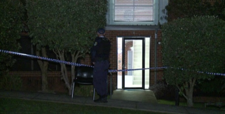 Police officer standing guard at a building sealed off with police tape.