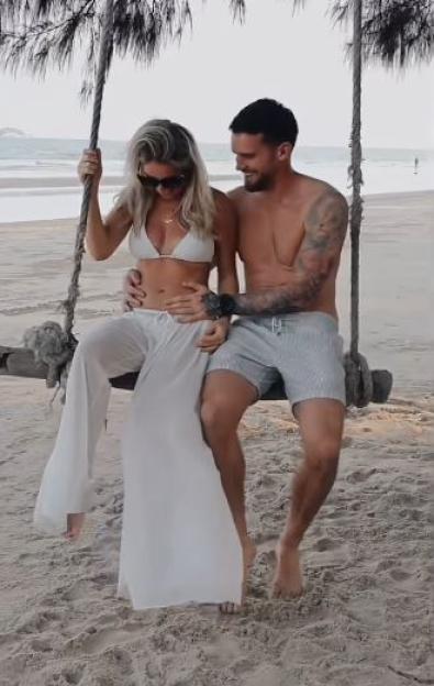 Gaz Beadle holding girlfriend Maia's baby bump as they sit on a beach swing.