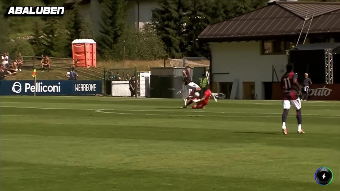 A soccer player in red tackles another player in white and black during a game.