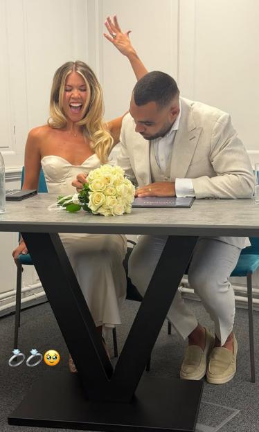 A man in a suit signing documents while a woman in a white dress shouts excitedly with her arm raised.