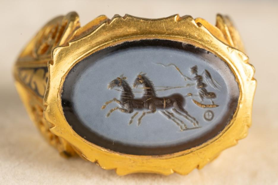 Gold ring with an intaglio carving of two horses pulling a chariot with a figure.