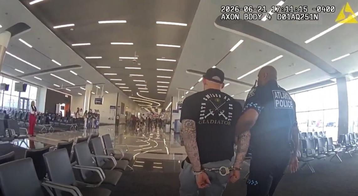 Dustin Poirier, in handcuffs, being escorted by an Atlanta police officer through an airport terminal.