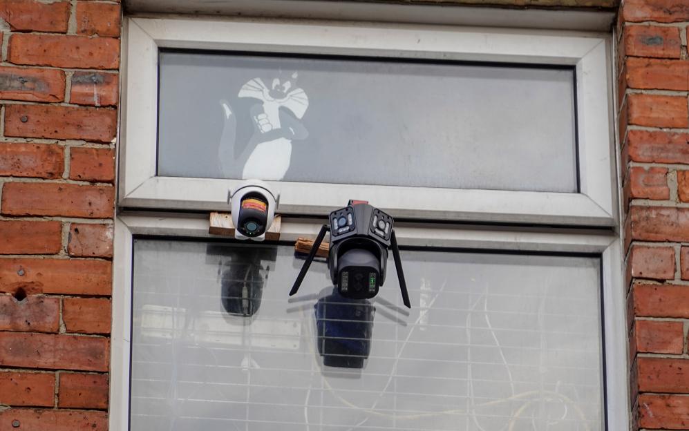 Two security cameras and a cartoon cat drawing on a window.