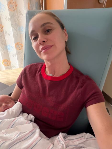 A woman in a red shirt holds a newborn wrapped in a striped blanket.