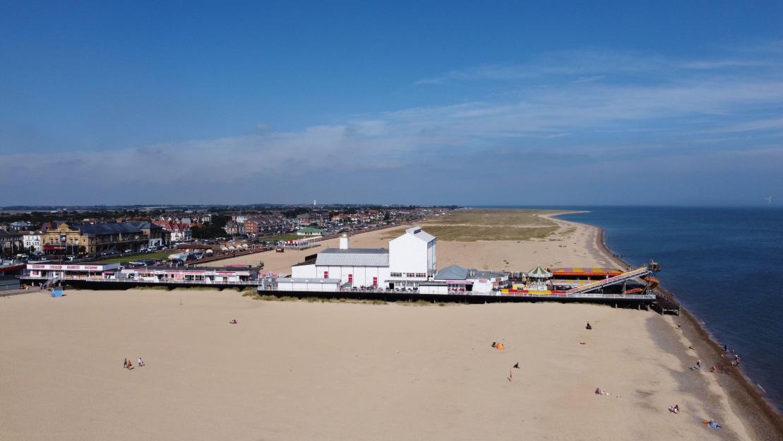 Aerial view of Great Yarmouth Britannia Pier with a sandy beach and buildings under a clear blue sky.