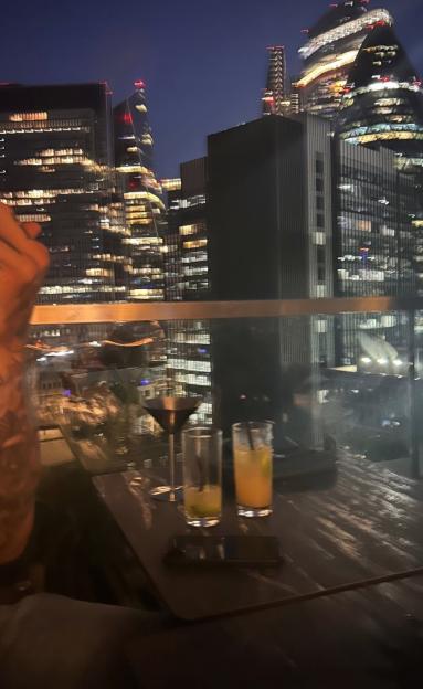An aerial shot of a city at night with three drinks on a glass table in the foreground.