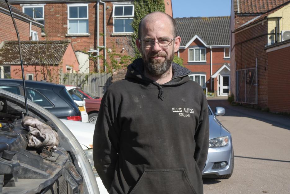 Ellis Speirs of Ellis Autos, standing in front of a partially open car hood and houses in Stalham.