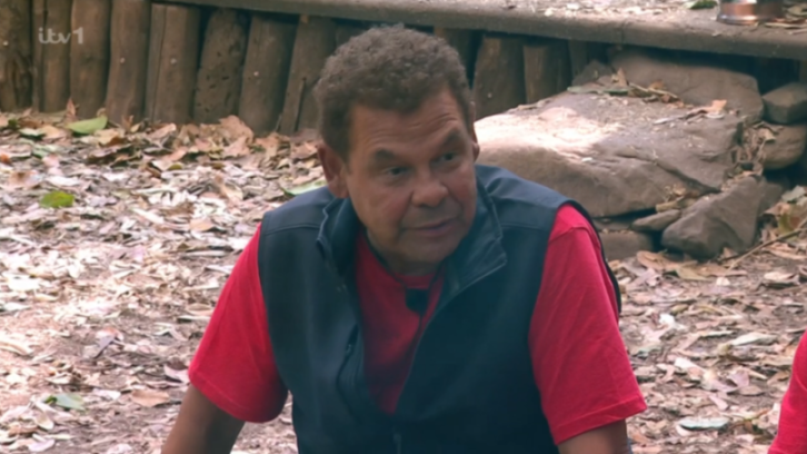 Man in a red shirt and dark blue vest looking slightly to the right.