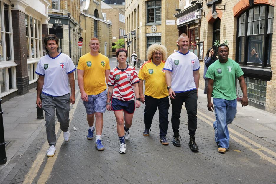 Six people in World Cup jerseys from different countries walk down a street.